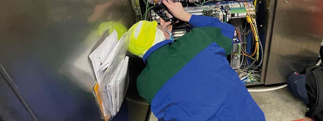 Technician inspecting electrical components and wiring inside an industrial cabinet.